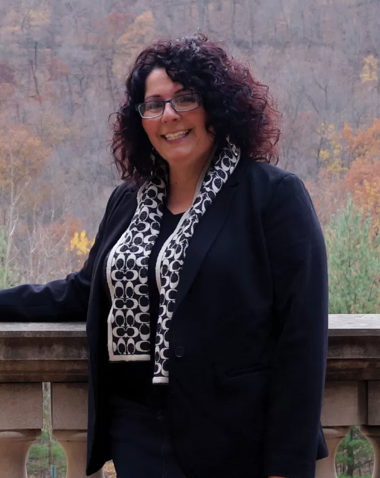 Dr. Carolyn Giannelli standing outdoors on a stone balcony overlooking autumn hills